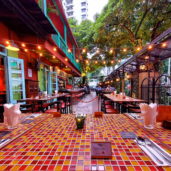 Outdoor Havana seating with colorful tiled tables, string lights, and surrounding trees.