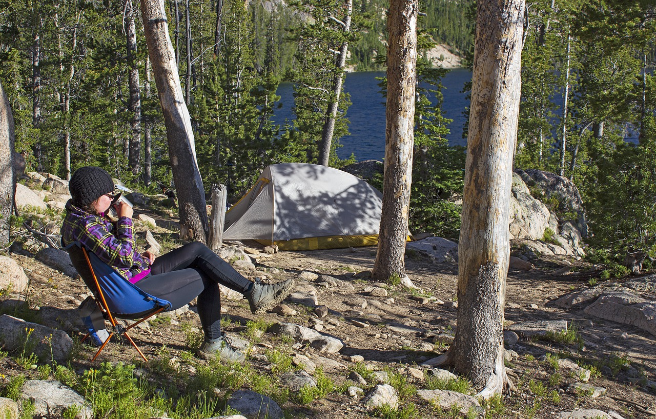 Woman drinking coffee on camp chair by dome tent in woods