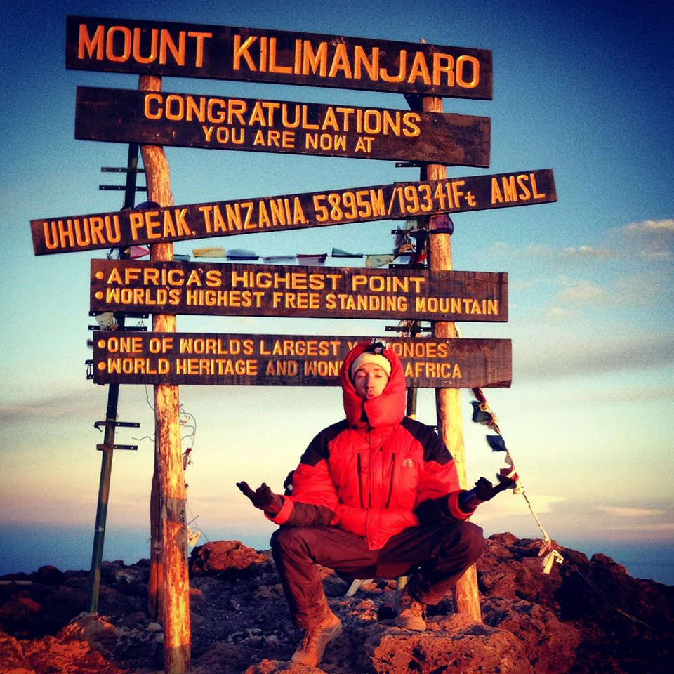 Man in a zen pose seated in front of sign at Uhuru Peak on Kilimanjaro