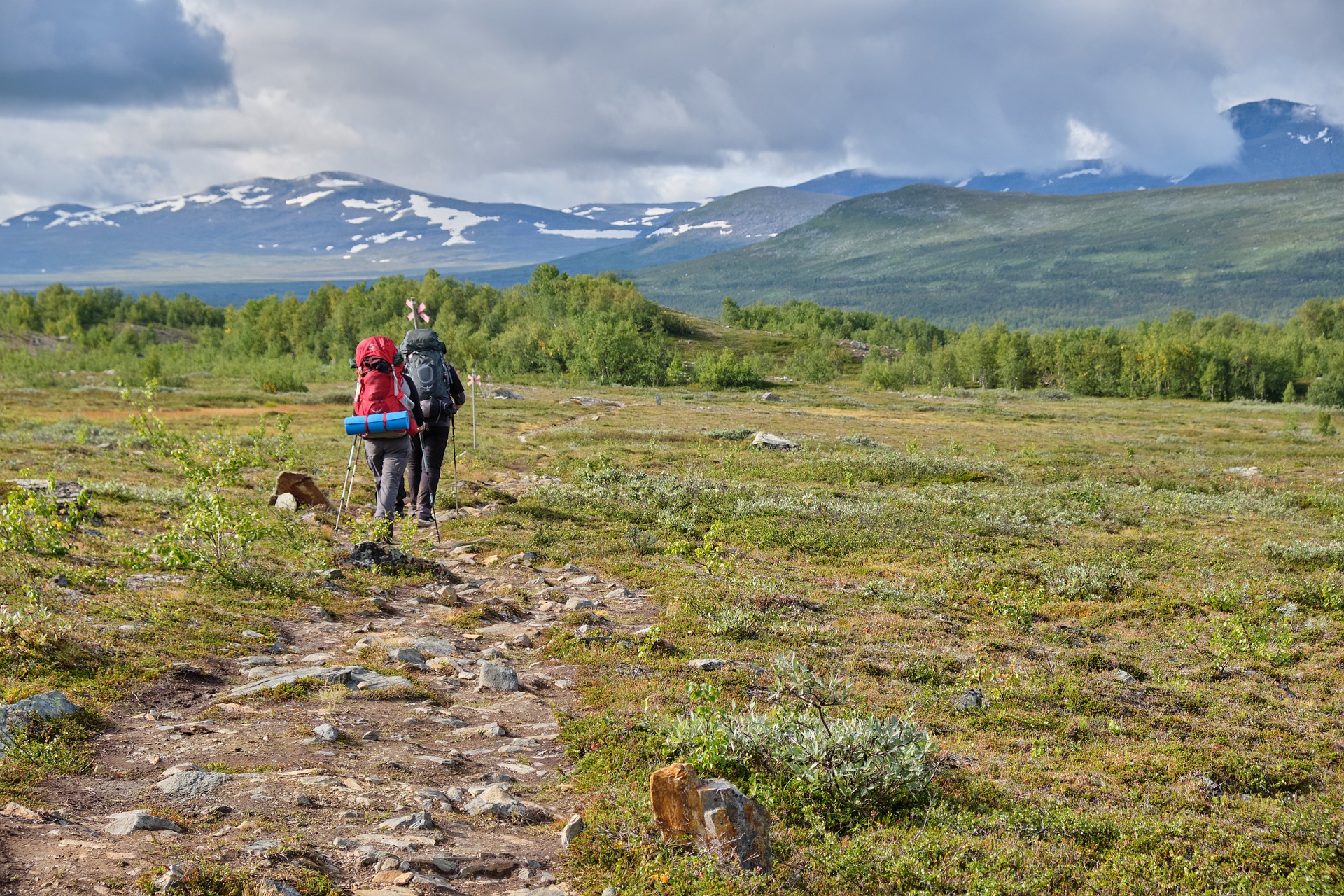 Two trekkers with rucksacks in green landscape among mountains