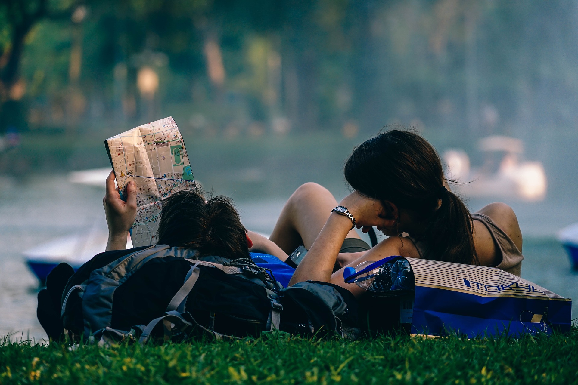 Asian couple with map lying on backpacks on grass