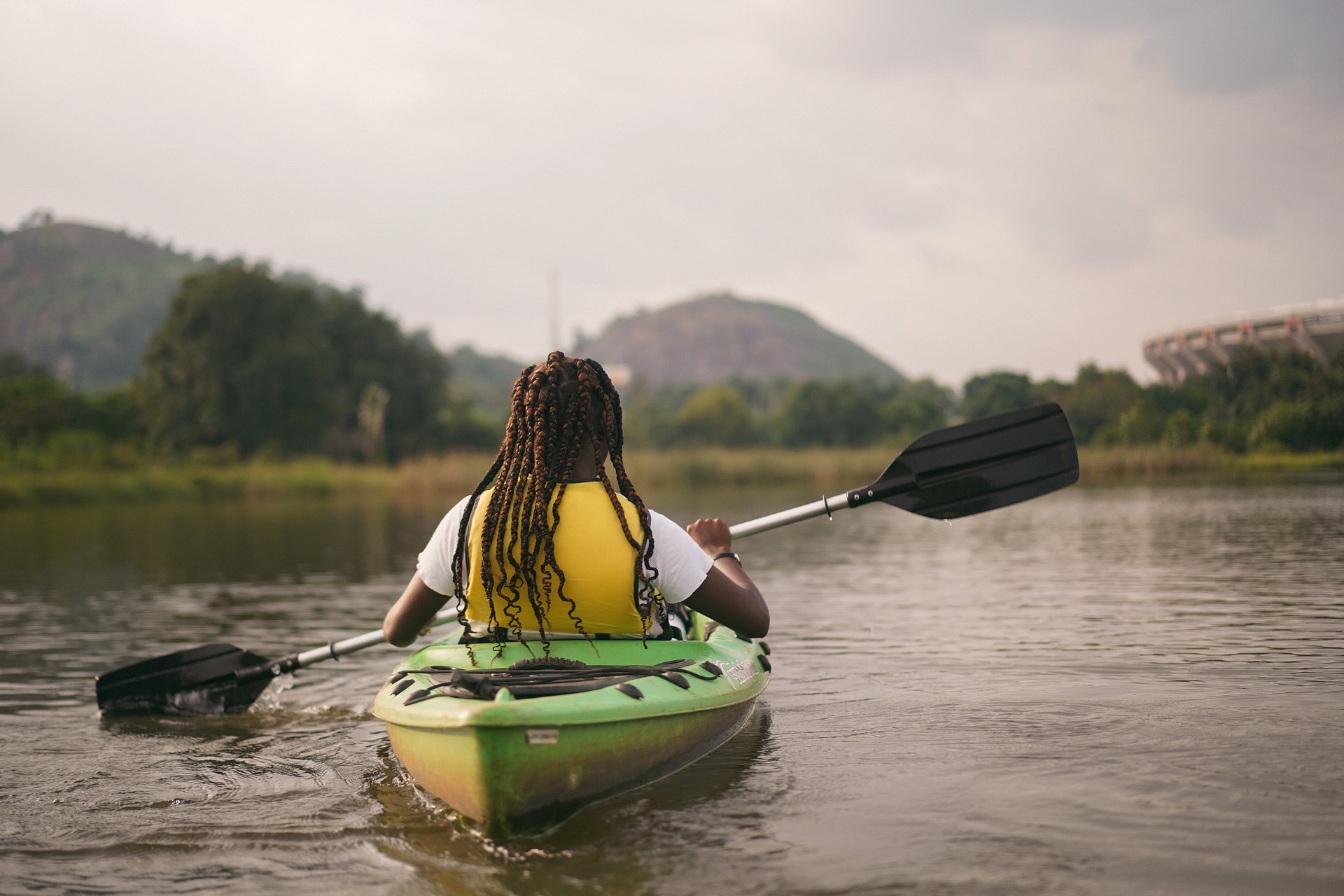 Black woman with braids in yellow life vest kayaking nature