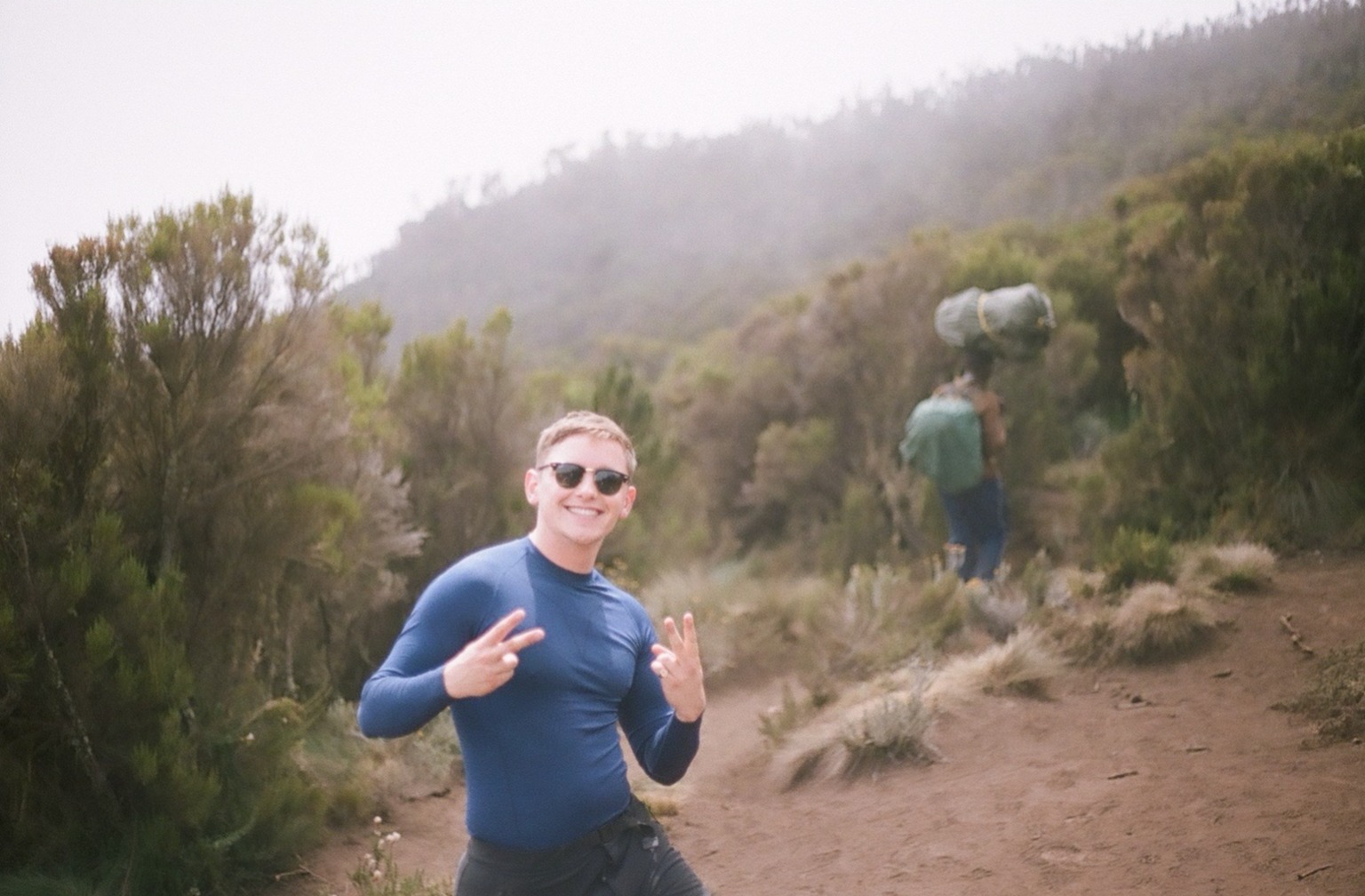 Jilian Tufokuji. Male hiker smiling at camera standing in moorland of Kilimanjaro