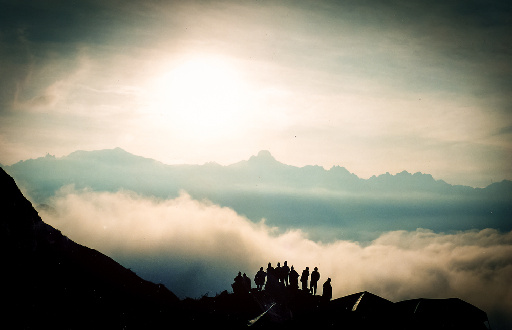 Ours. Silhouette of group of Inca Trail trekkers standing with Andes mountains behind them and clouds below