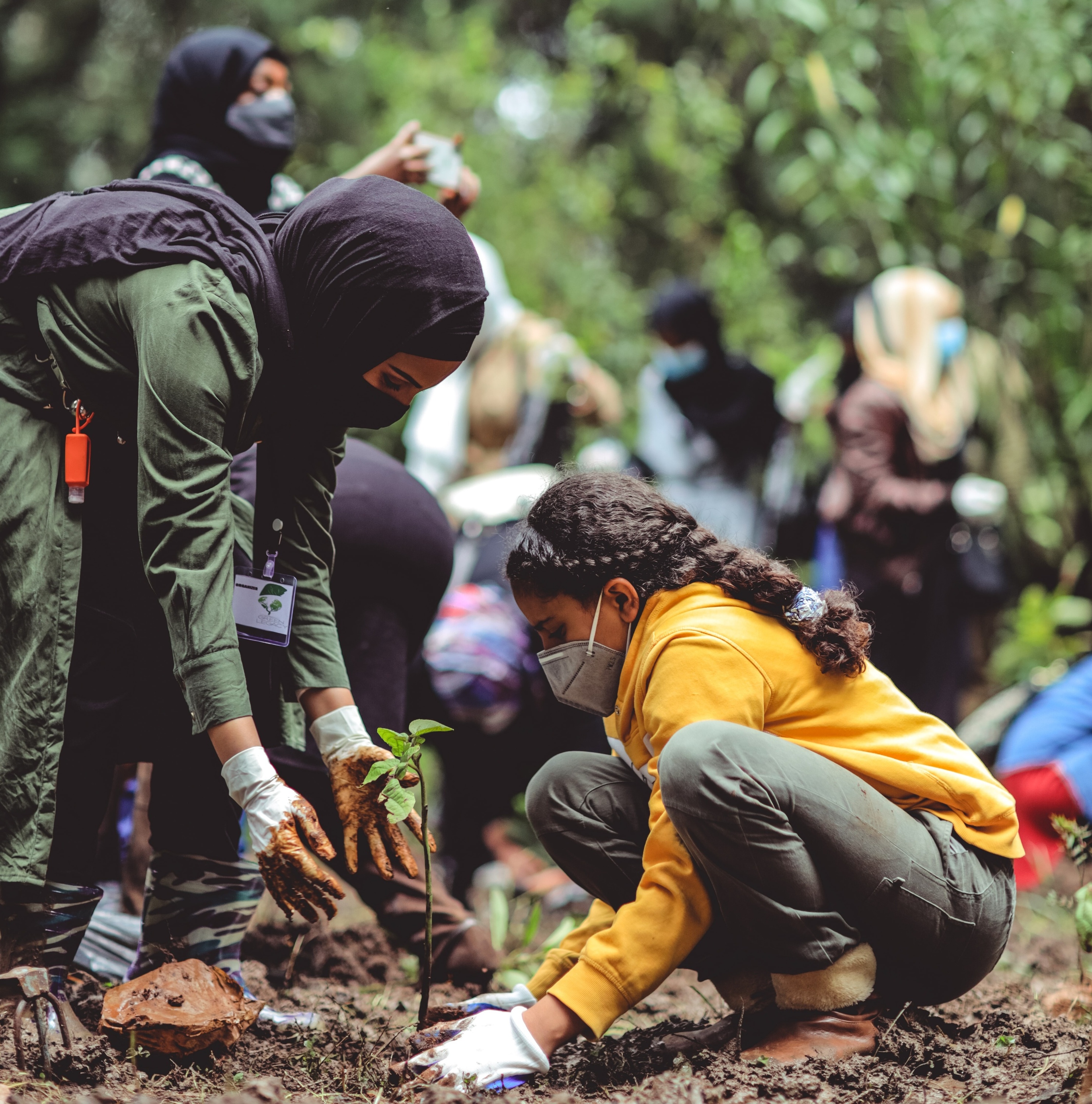 Muslim mother and daughter with yellow jacket and face mask planting a tree