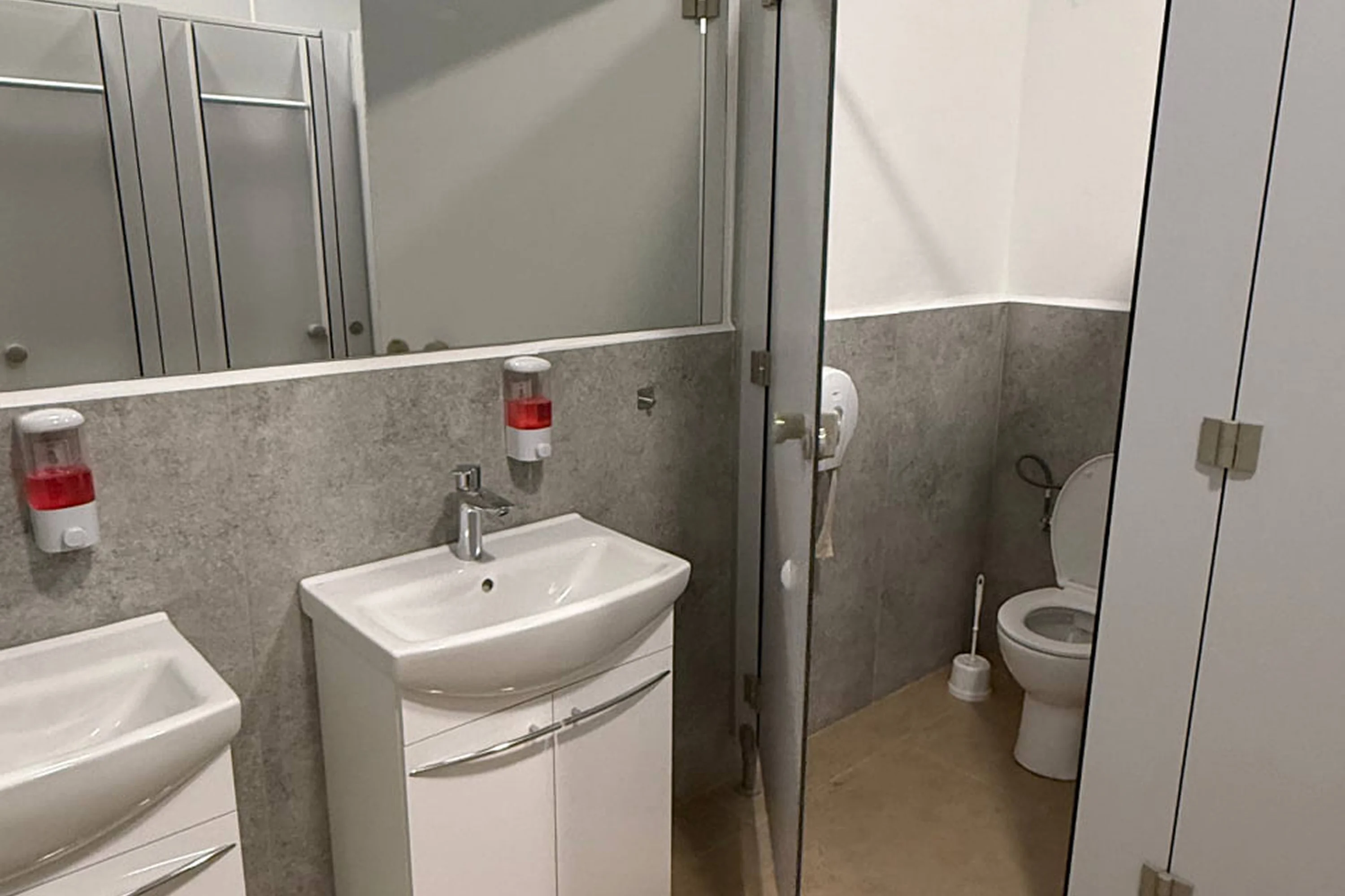 Modern clean public restroom with white sinks, soap dispensers, and a toilet stall with an open door.