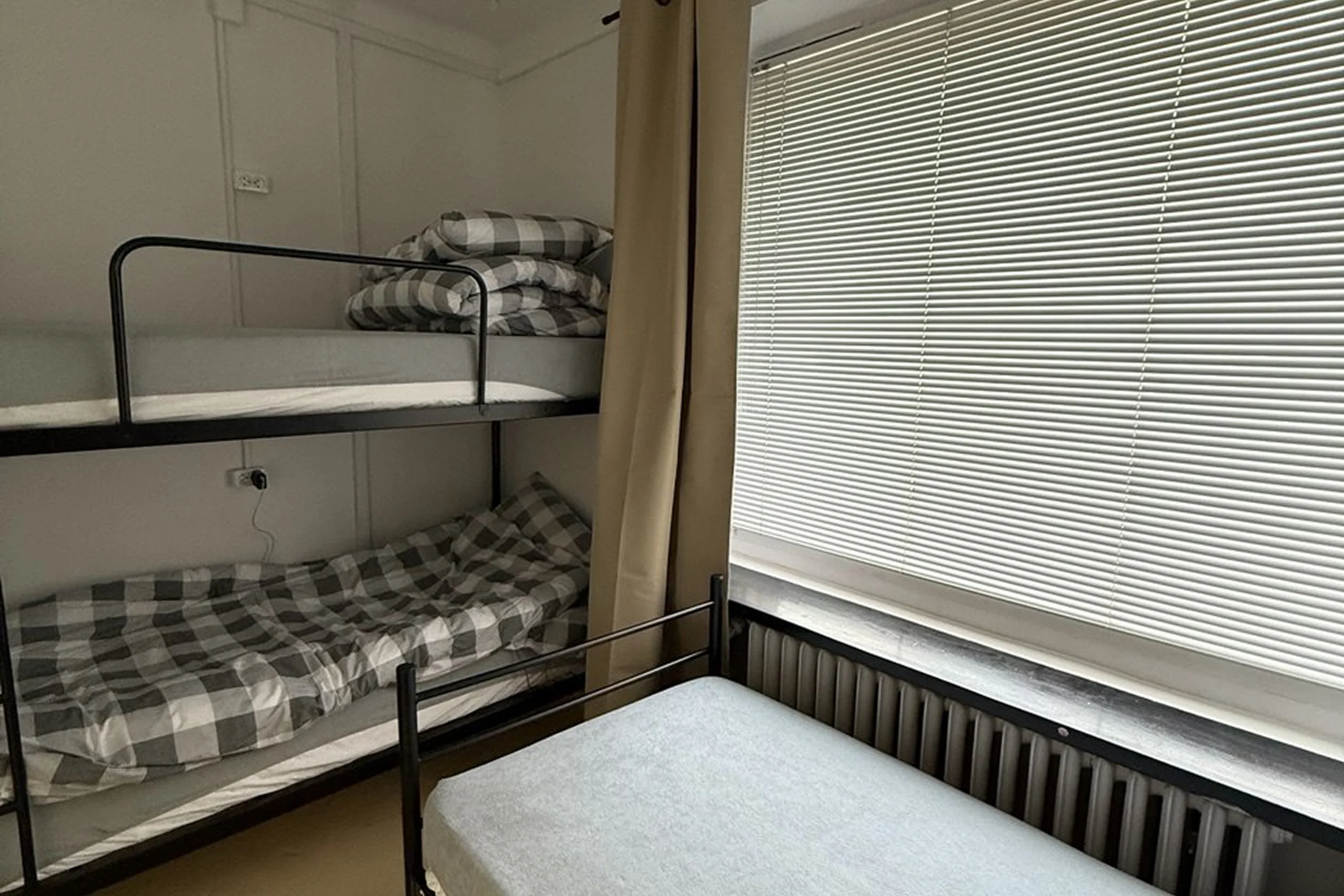 Small room with a black metal bunk bed and a single bed near a window covered with closed horizontal blinds.
