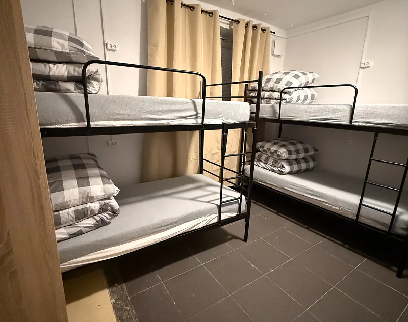 Small room with two black metal bunk beds with gray checked bedding and beige curtains on the window.