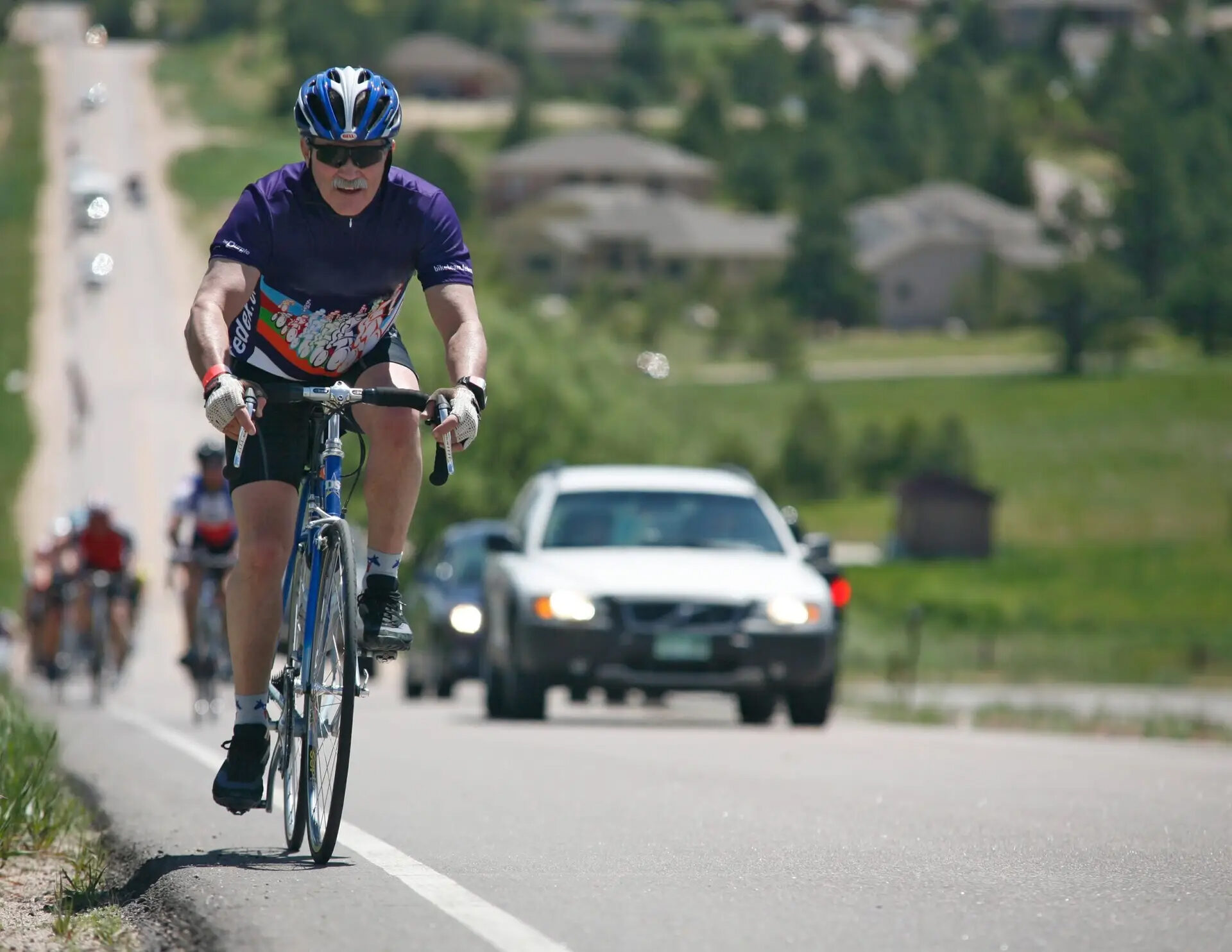 Road cyclist riding on a Colorado roadway with a car following closely behind