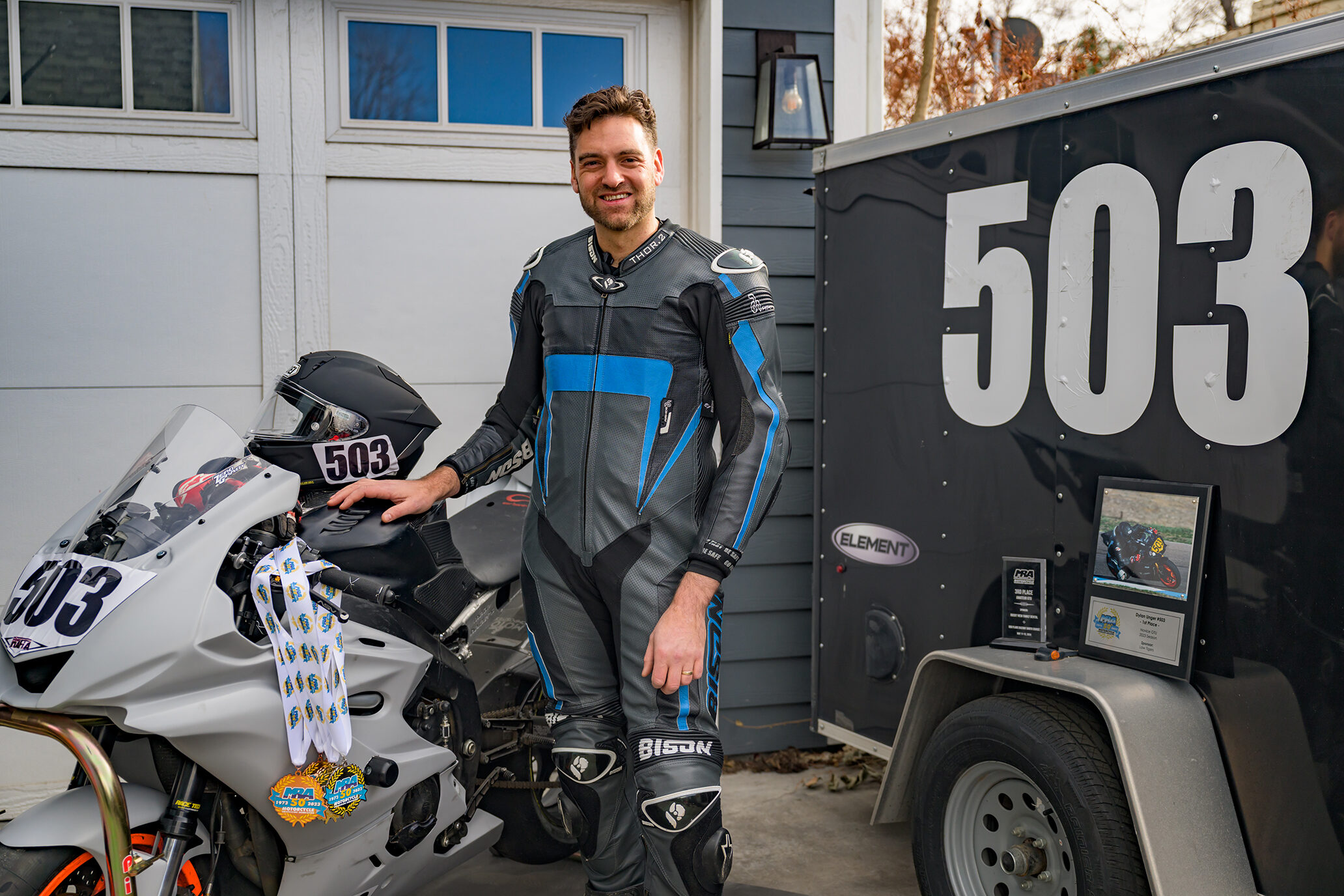 Dylan Unger in race leathers next to his #503 race bike, with MRA season medals and plaques