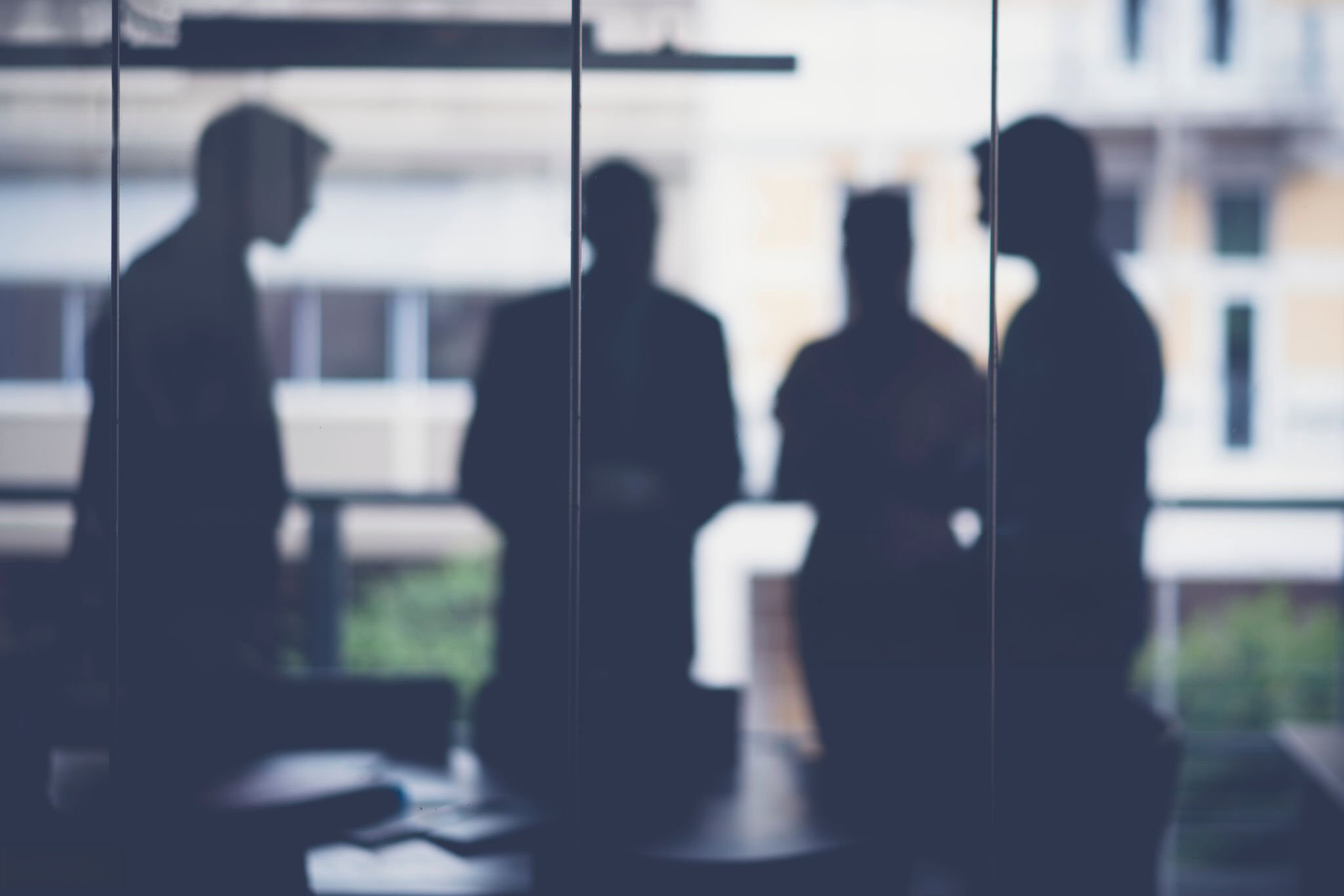 Silhouetted figures behind frosted glass, suggesting an insurance carrier's back-room claim decisions