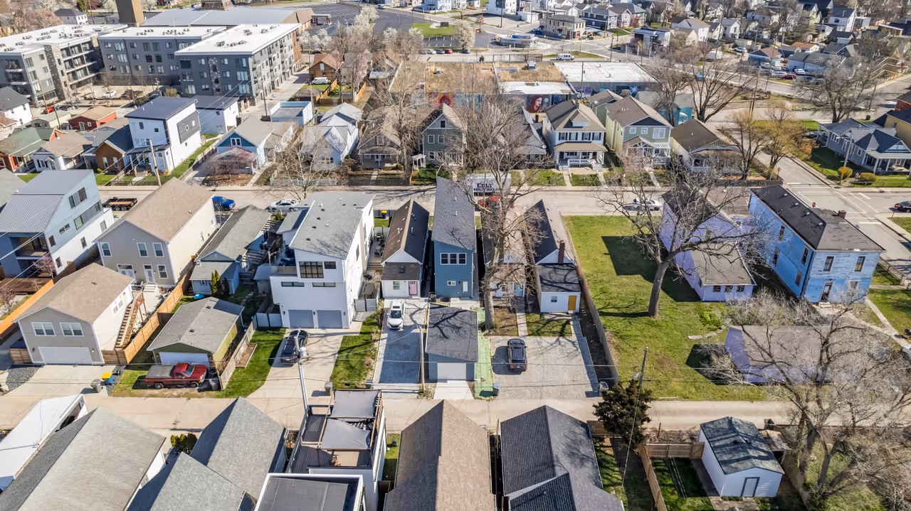 Aerial view of a residential neighborhood with houses, driveways, cars, and leafless trees on a clear day.