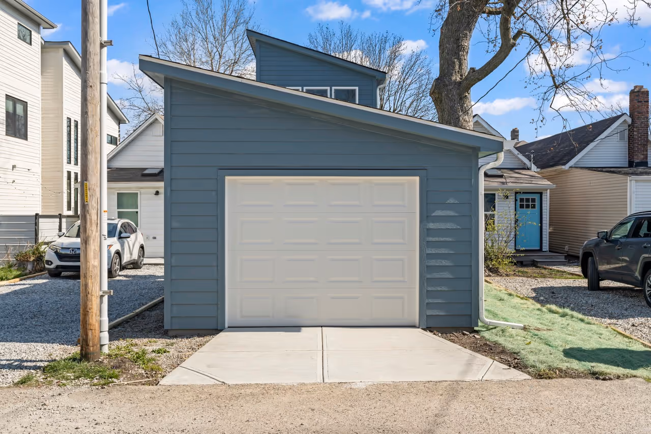 Blue detached garage with a white door in a residential area under a clear sky.