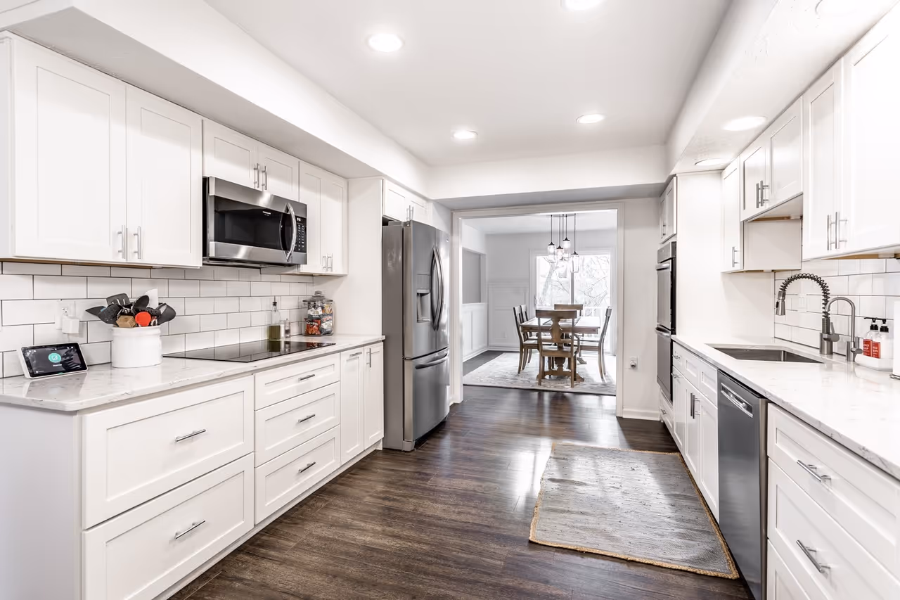 Modern bathroom with white marble floor, wooden vanity with sink, large mirror, and bathtub with black tile walls.