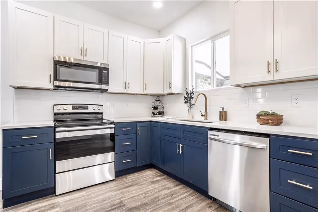 Modern kitchen corner with glossy gray cabinets, stainless steel microwave, gas stove, toaster, knife set, air fryer, and white countertops.
