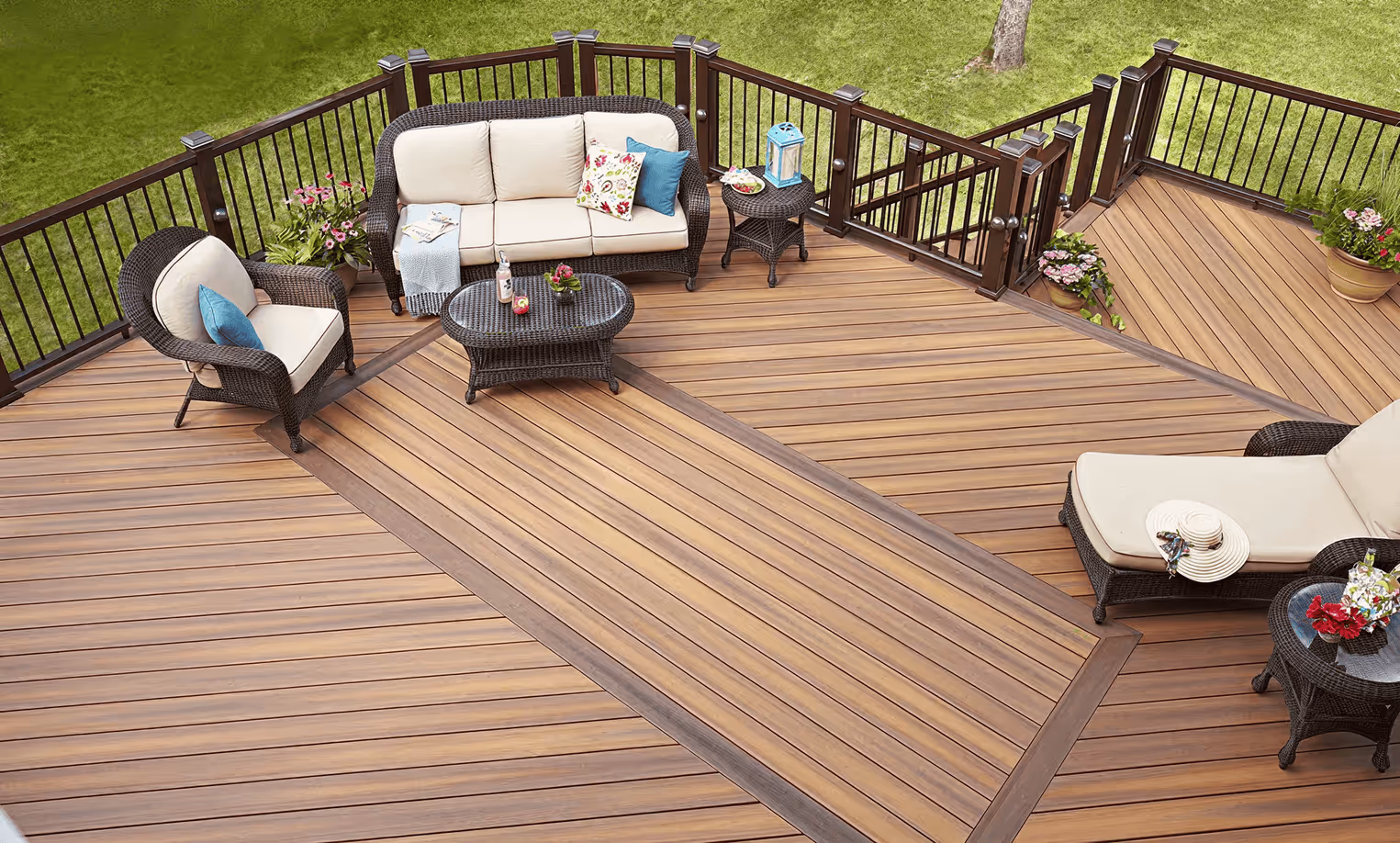 Spacious outdoor wooden deck with dark wicker sofa, armchair, chaise lounge, coffee tables, and potted flowers.