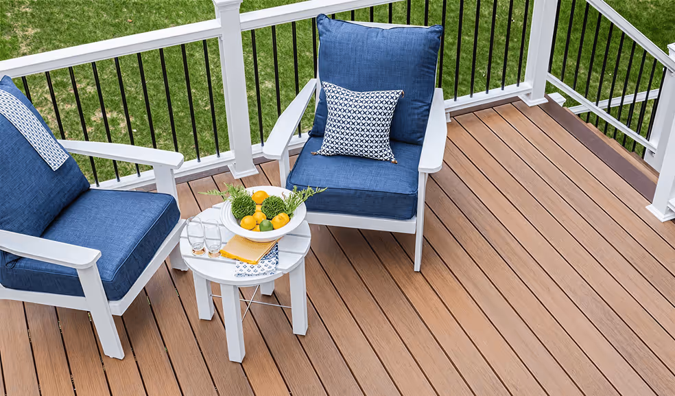 Two white patio chairs with blue cushions and a small white round table holding a bowl of lemons and decorative greenery on a wooden deck.