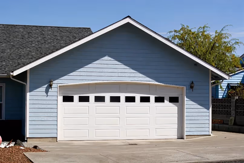 Blue house with a white double garage door under a pitched roof on a sunny day.