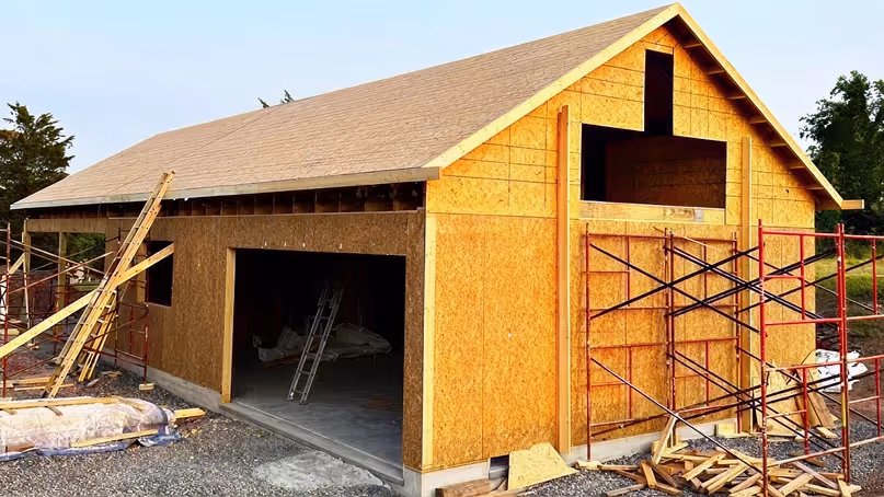 Wooden garage under construction with scaffolding and ladders around unfinished exterior walls.
