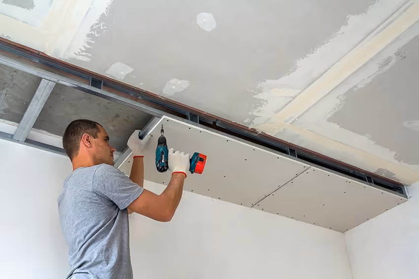 Man installing drywall ceiling panels using a cordless drill.