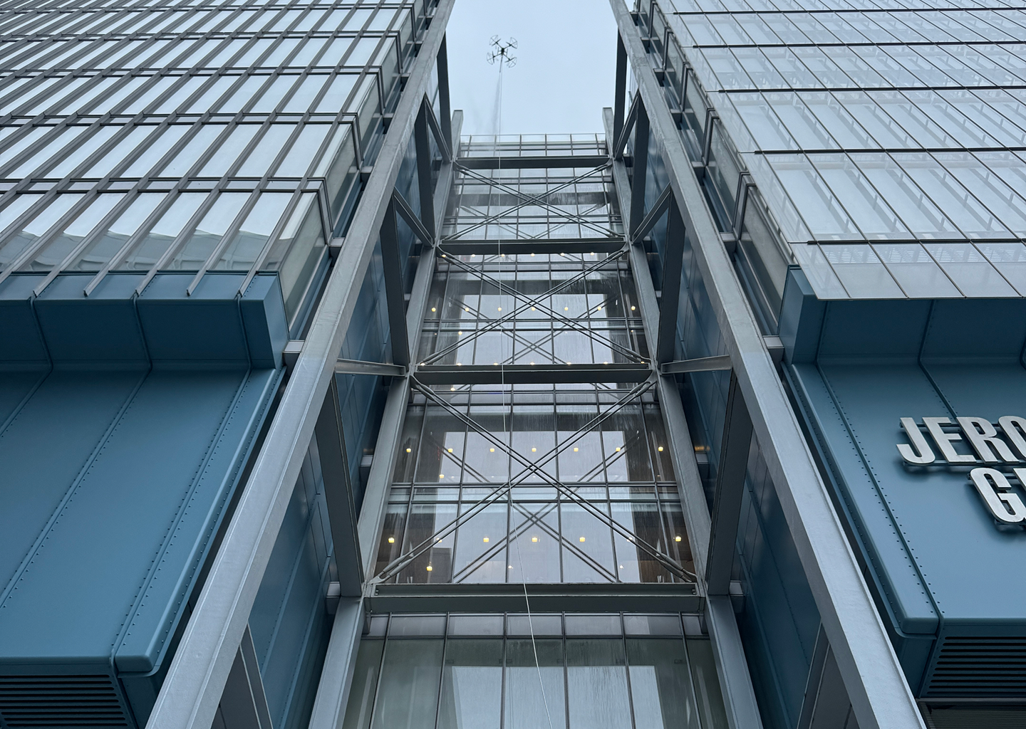 Upward view of modern glass and steel high-rise building with structural cross braces and blue paneling.