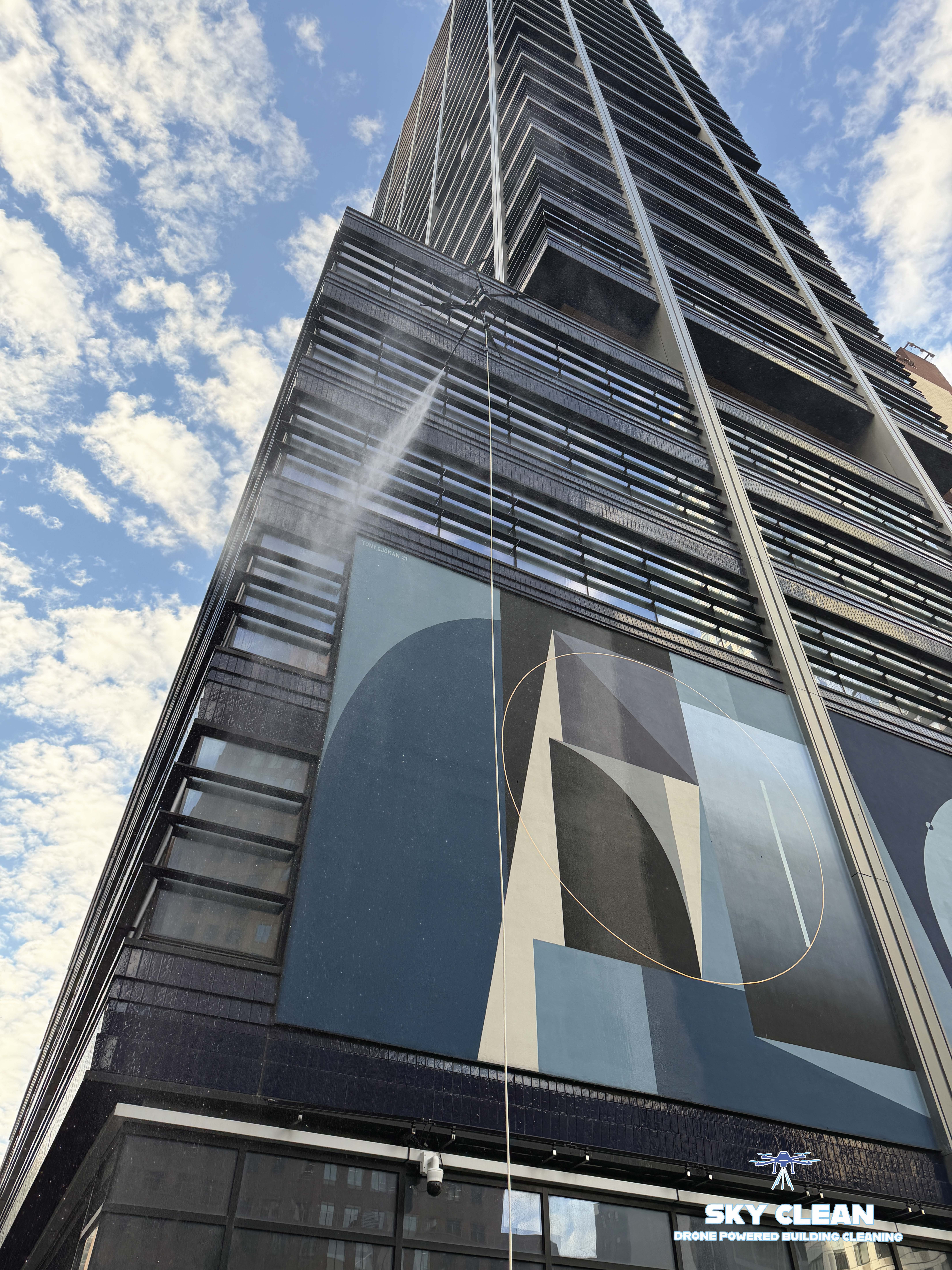 Modern high-rise building viewed from below with abstract geometric mural and blue sky with clouds.