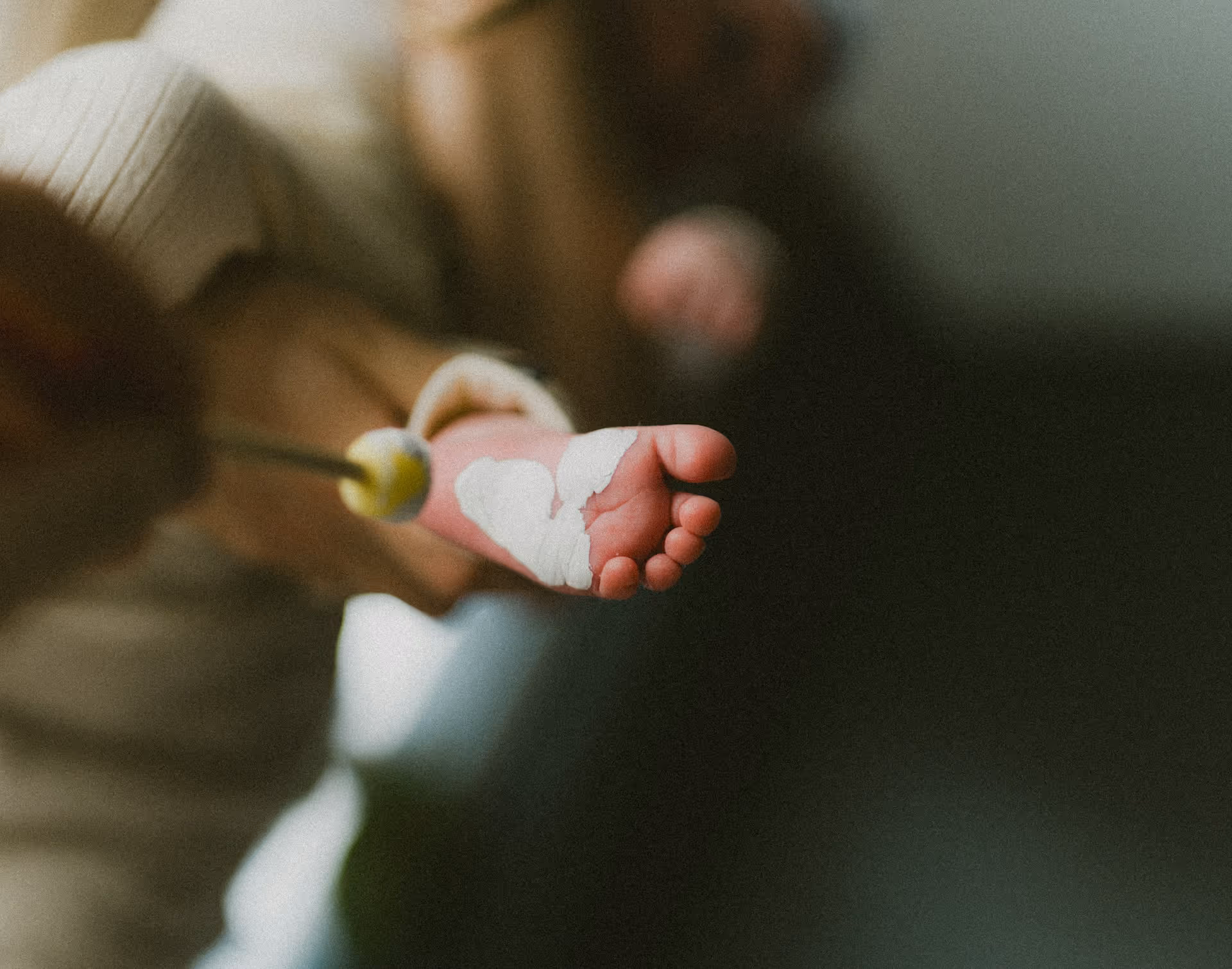 Close-up of an adult hand painting a white heart shape on a baby's foot.