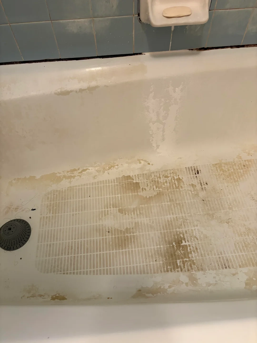 Bathtub with peeling, discolored, and stained surface and blue tiled wall with soap holder in Casa Adobes, AZ