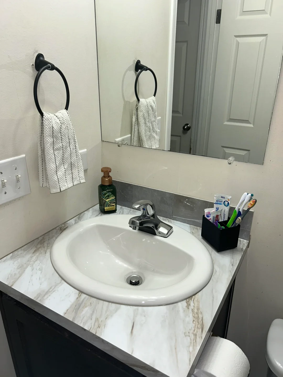 Bathroom sink with a chrome faucet, hand soap dispenser, toothbrush holder with toothbrushes and toothpaste, and a towel hanging on a black ring in Tucson, AZ