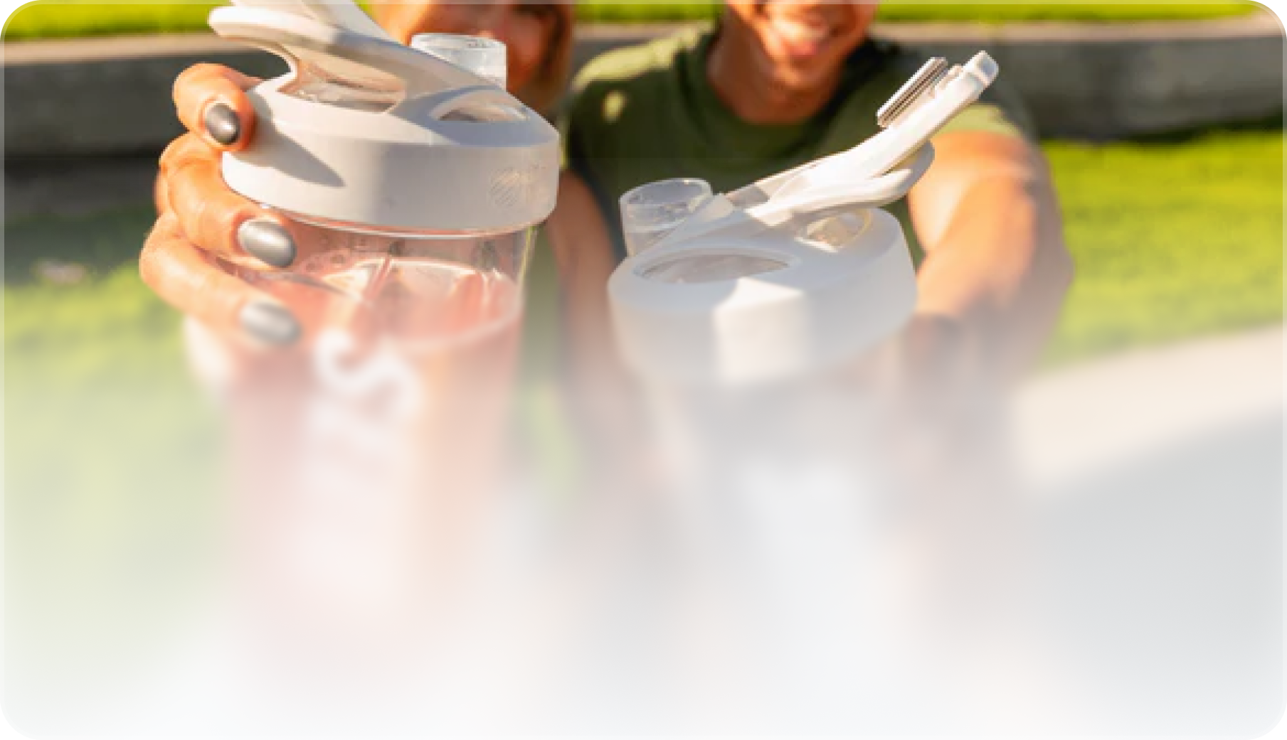 Two people outdoors holding up white-lidded shaker bottles with clear liquid inside, smiling in bright sunlight.