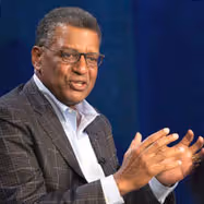 Man wearing a red tuxedo jacket with black lapels, a white shirt, and a red bow tie, standing indoors with a neutral expression.