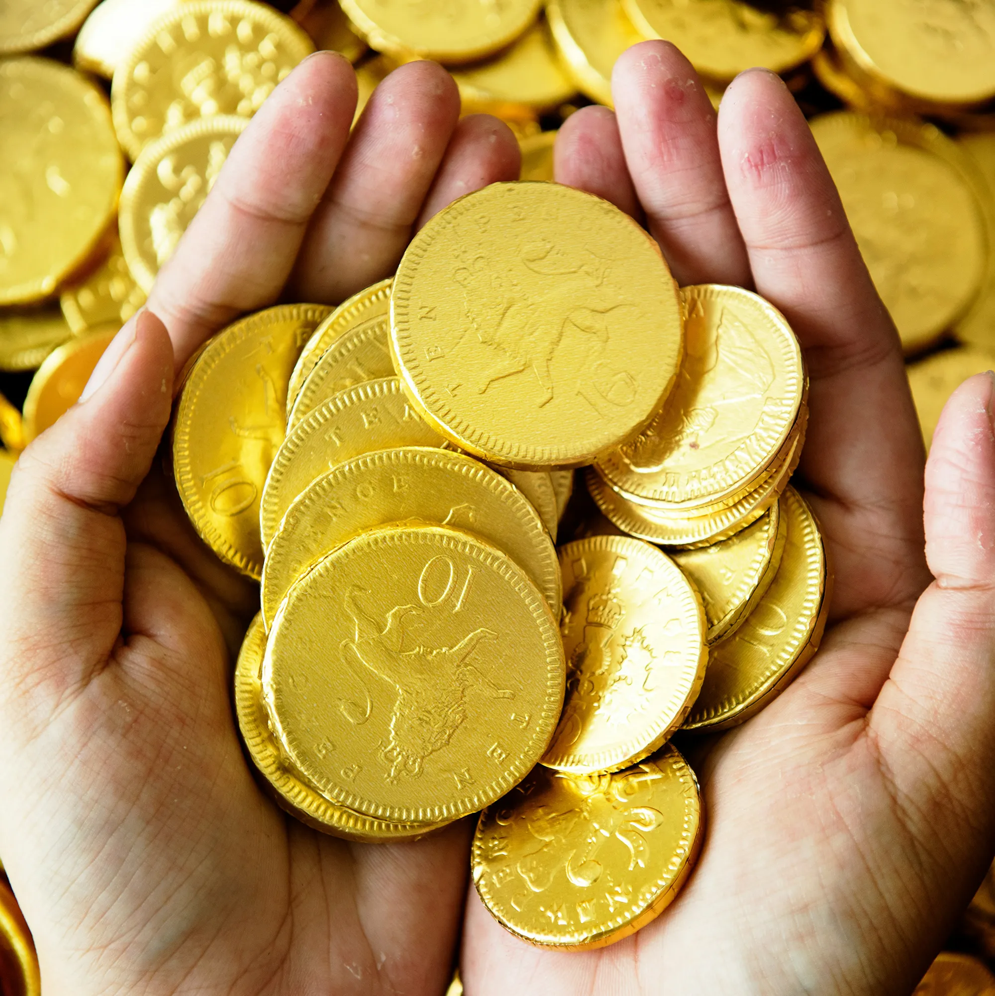 Två händer som håller i guldmynt med choklad i under skattjakt.