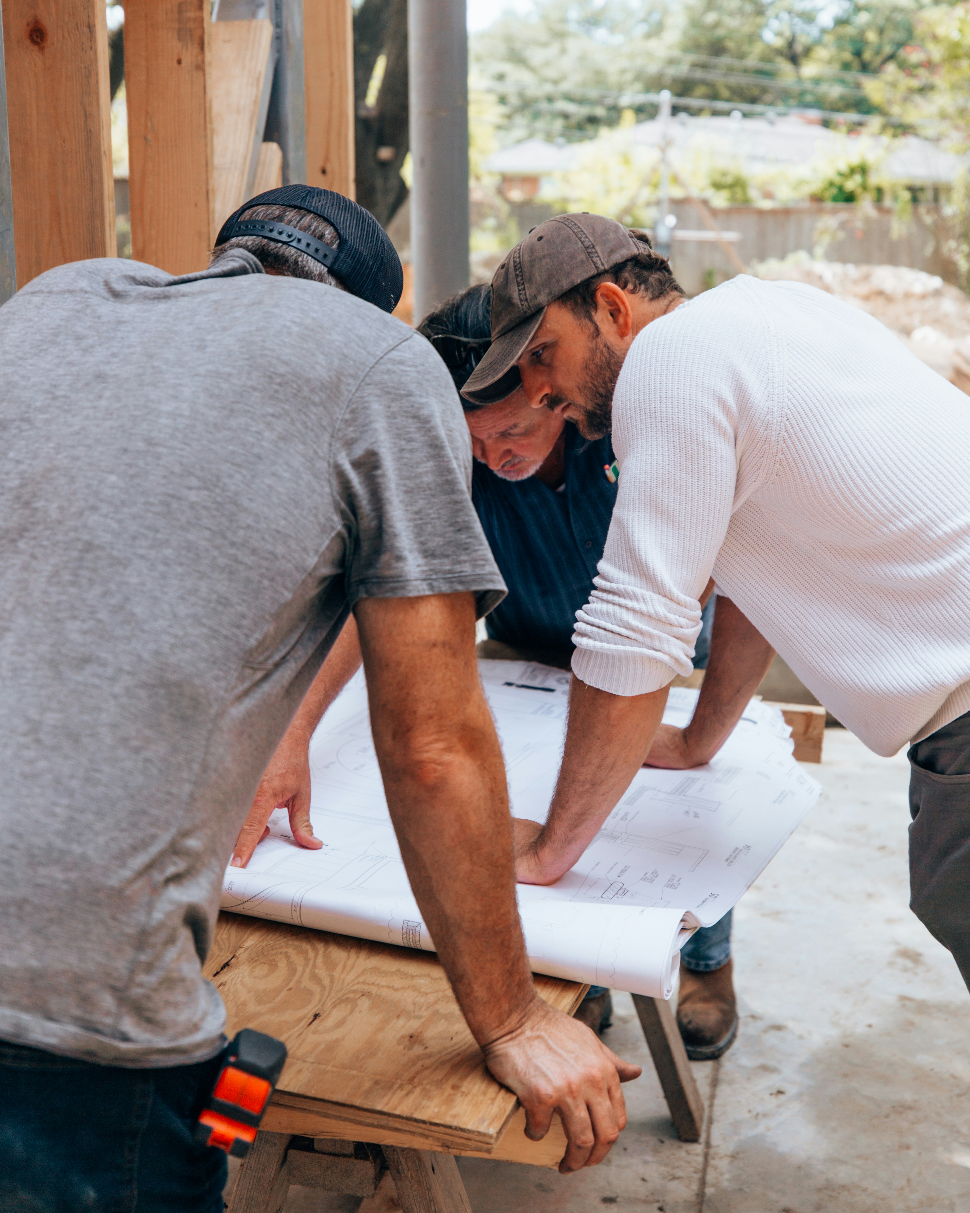 Three business owners reviewing architectural blueprints at a construction site.