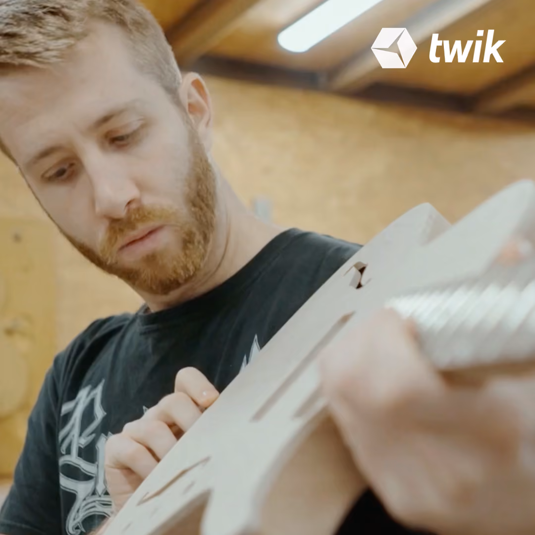 Bearded man closely inspecting and working on a wooden guitar body in a workshop.