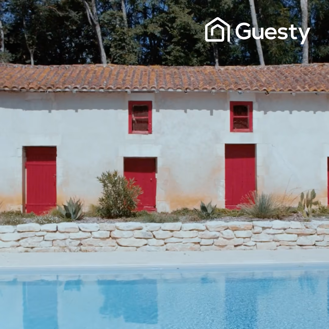 White building with red doors and windows reflected in a clear blue swimming pool in front.