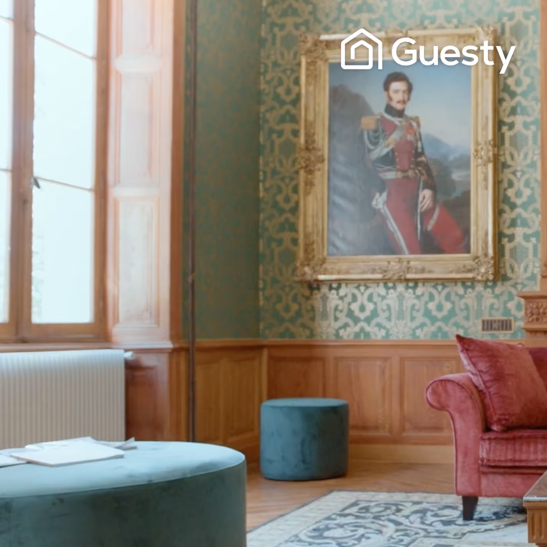 Luxurious living room with green patterned wallpaper, framed portrait, teal ottomans, and a red velvet sofa.