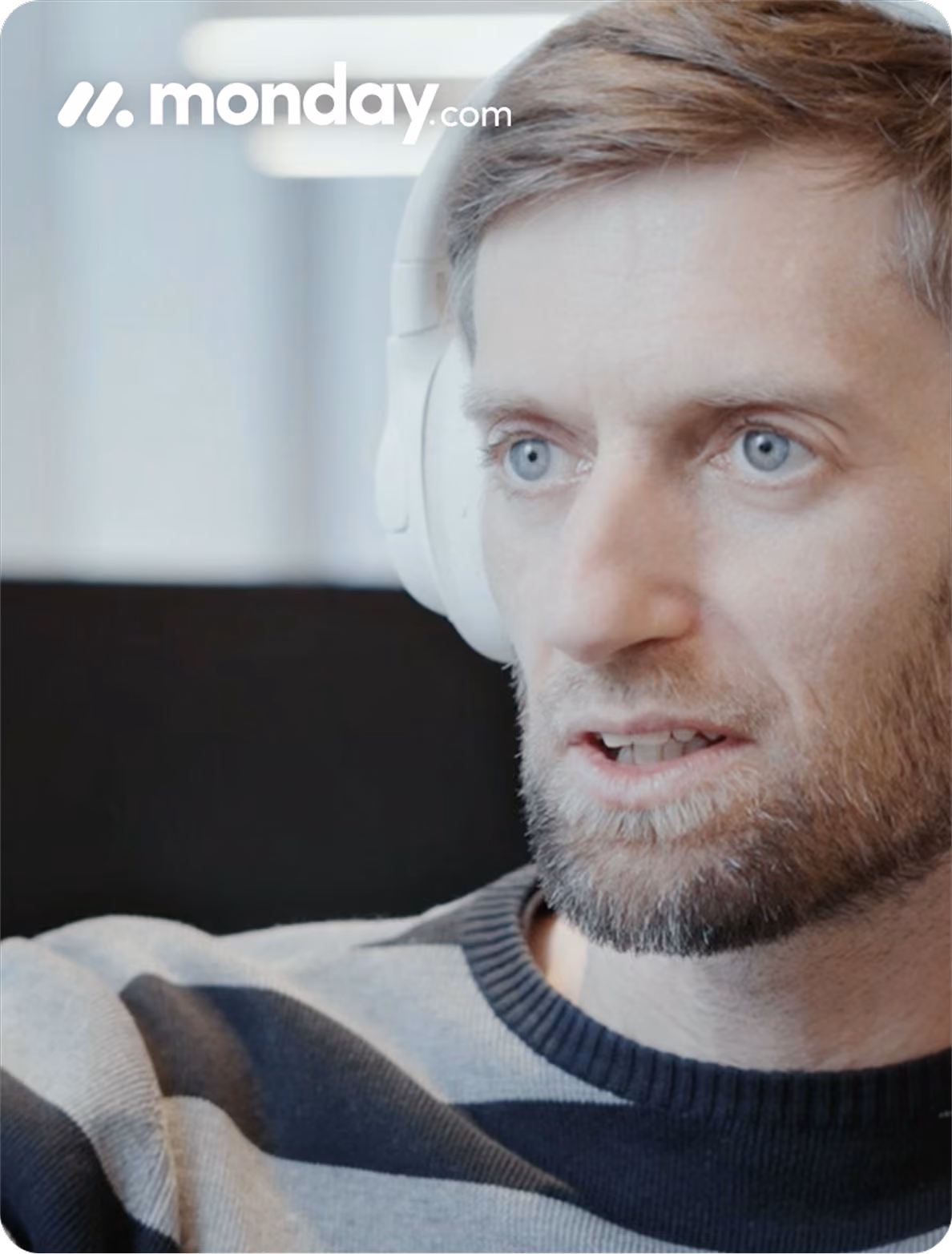 Close-up of a man with blue eyes and beard wearing white headphones and a striped sweater.