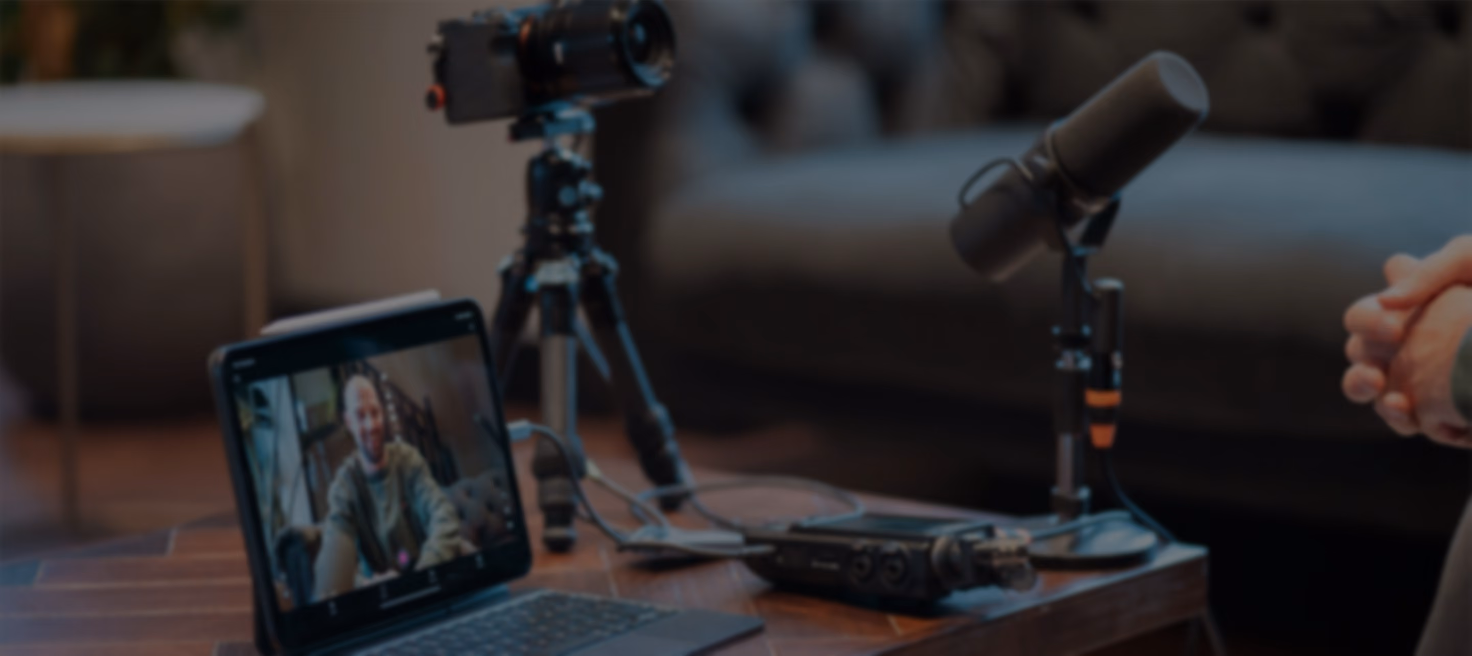 Podcast setup with microphone, camera on tripod, and tablet showing a video call with a man.