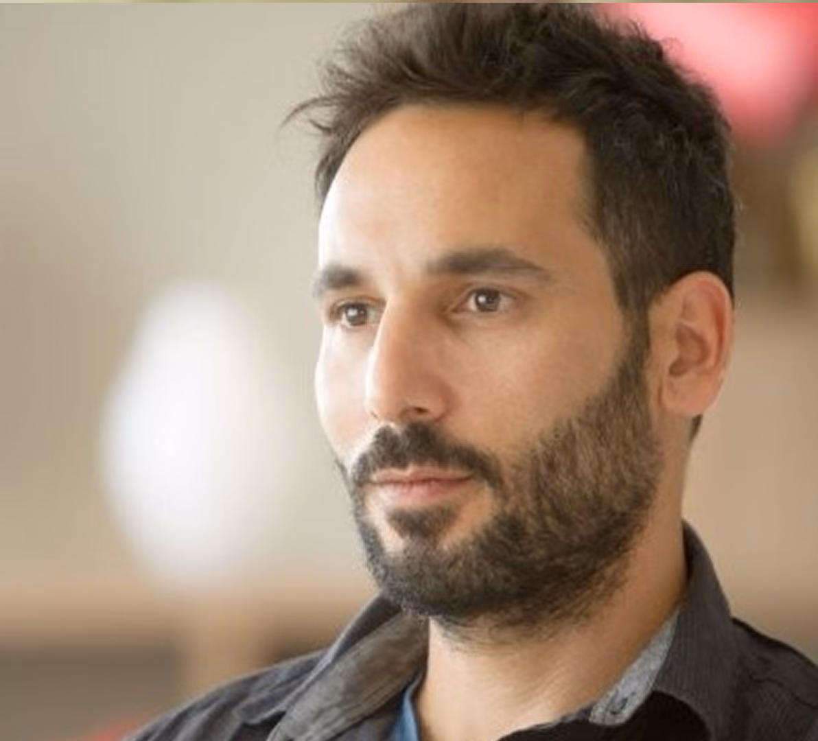Portrait of a thoughtful young man with short dark hair and a beard looking slightly to the side.