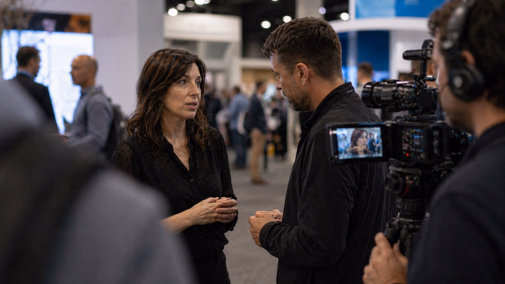 A woman and a man face each other talking while a cameraman films them at an event.