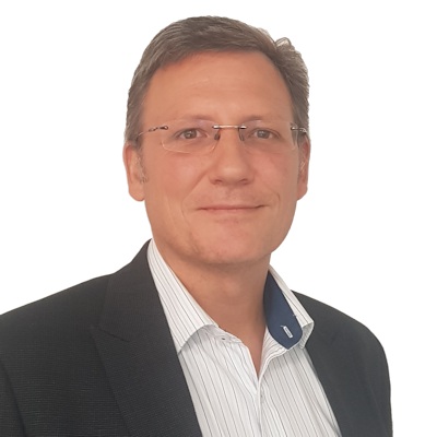 Man with short brown hair and glasses wearing a dark blazer and white striped shirt.