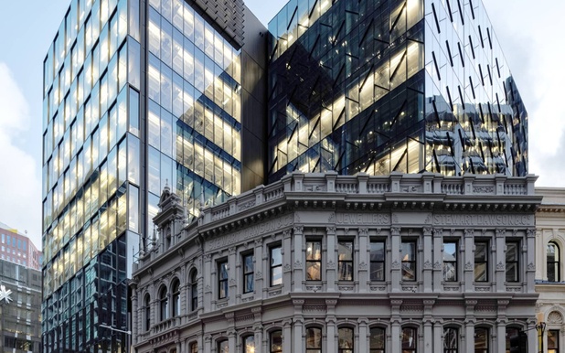 Modern glass skyscraper reflecting light behind an ornate historic stone building at dusk.