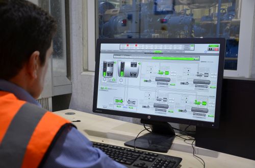 Man in safety vest monitoring industrial refrigeration system control panel on computer screen.
