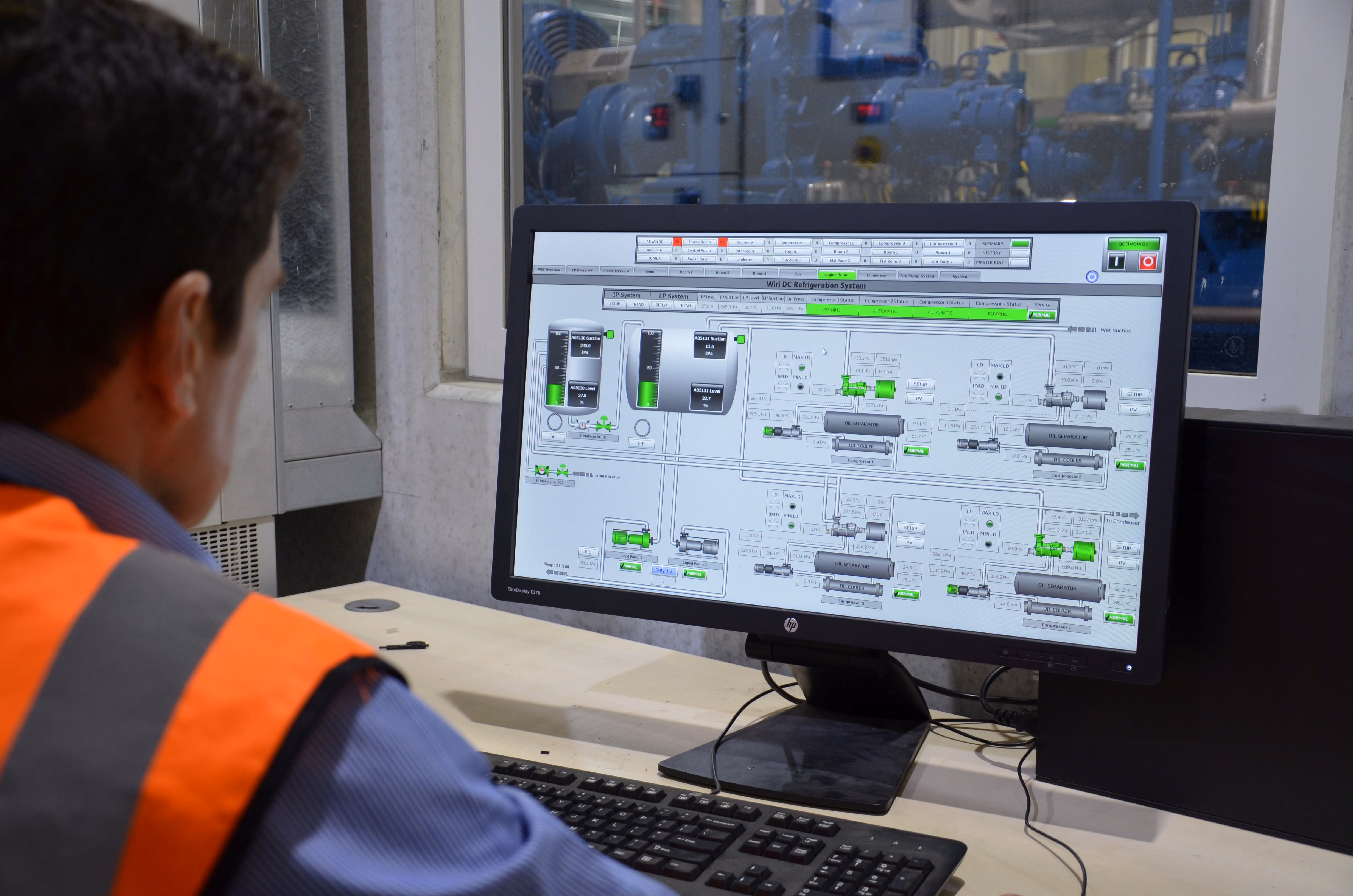Man in safety vest monitoring industrial refrigeration system control panel on computer screen.