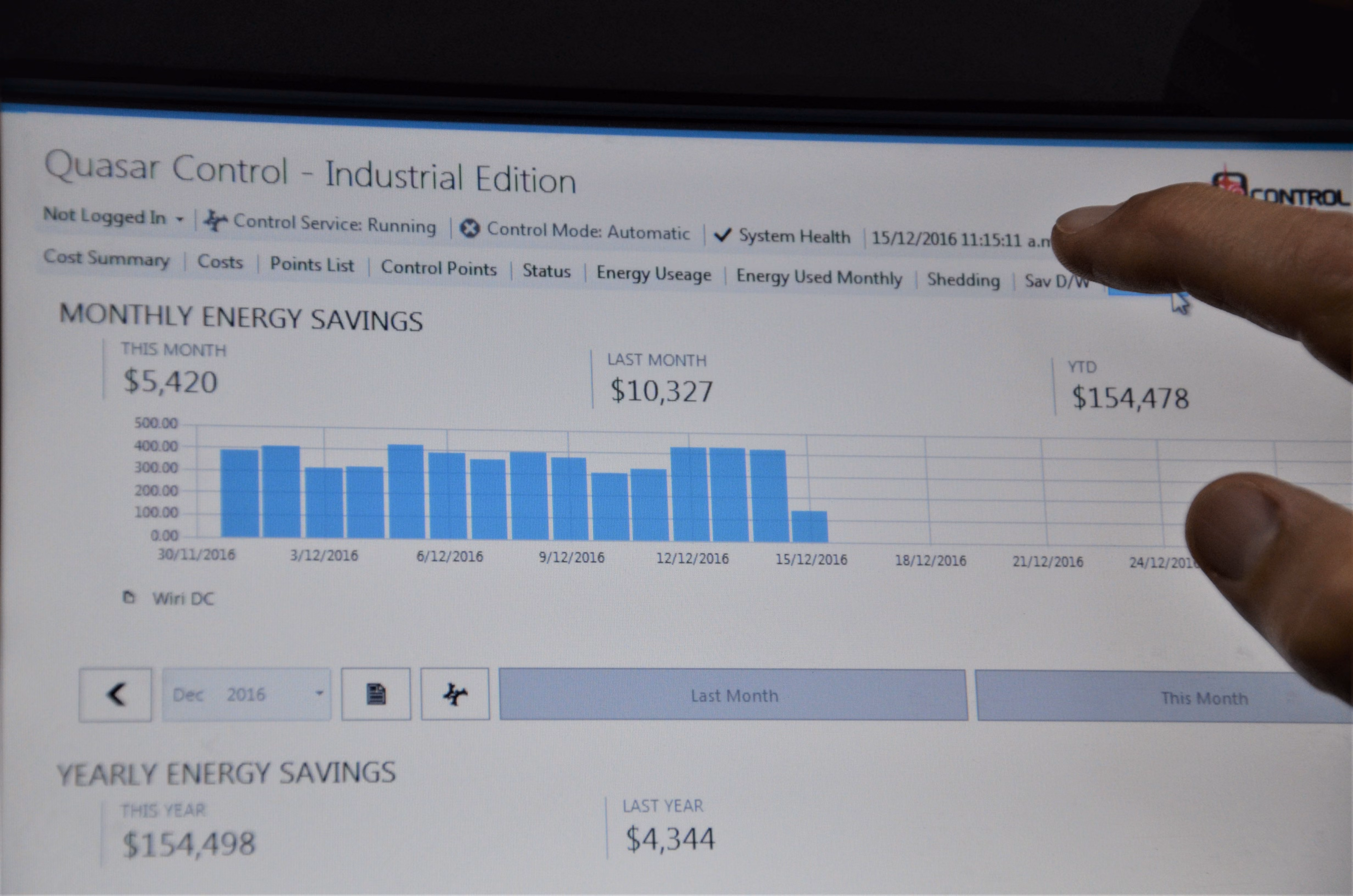 Screen of Quasar Control showing monthly and yearly energy savings with bar graph and a hand pointing at the screen.