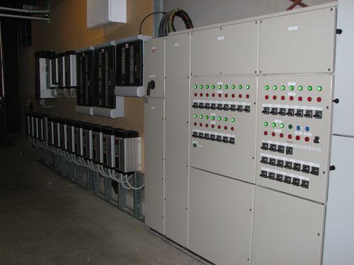 Industrial electrical control panels with switches, indicator lights, and multiple connected devices on a wall.