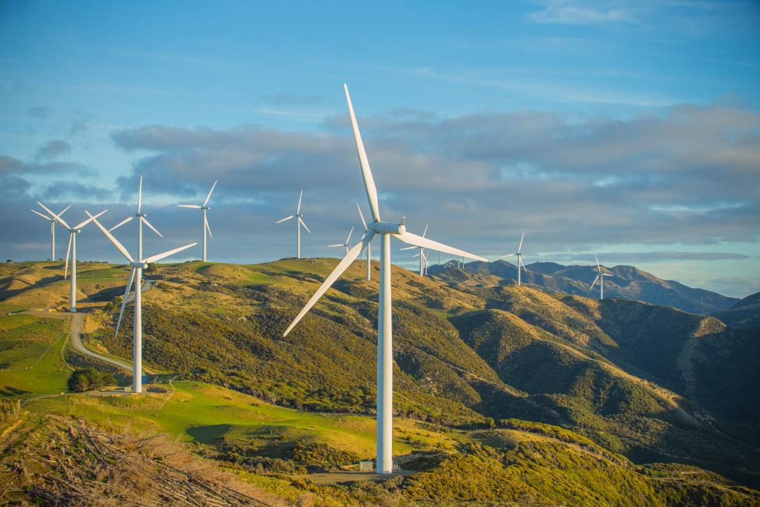 Wind turbines on green hills under a partly cloudy blue sky during daylight.