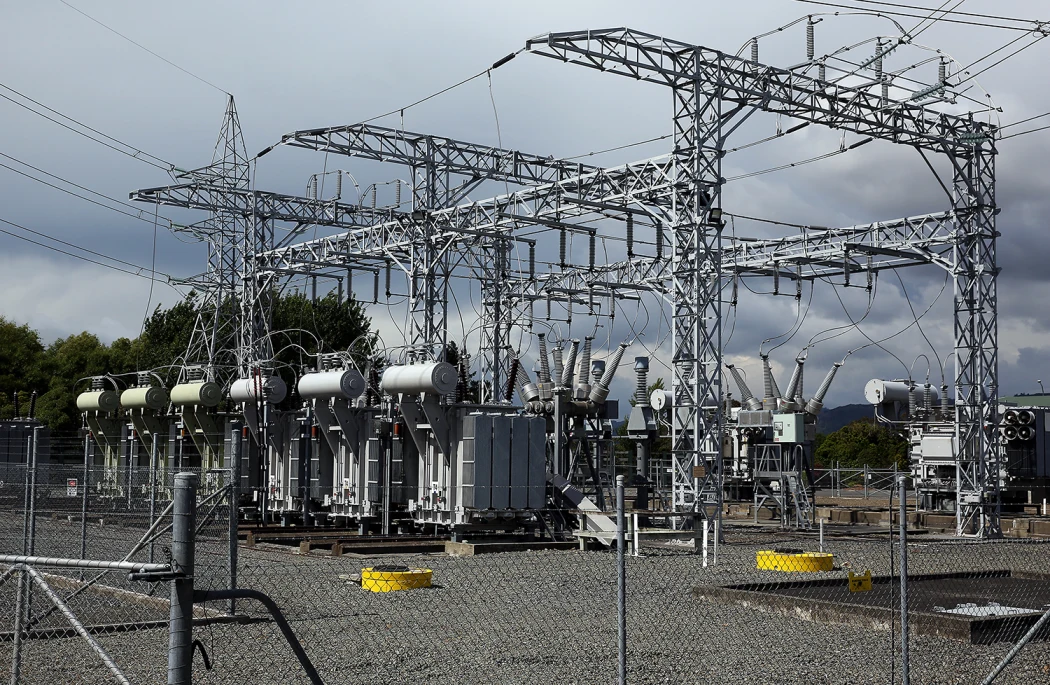 Electrical substation with transformers, cables, and metal frameworks under a cloudy sky.