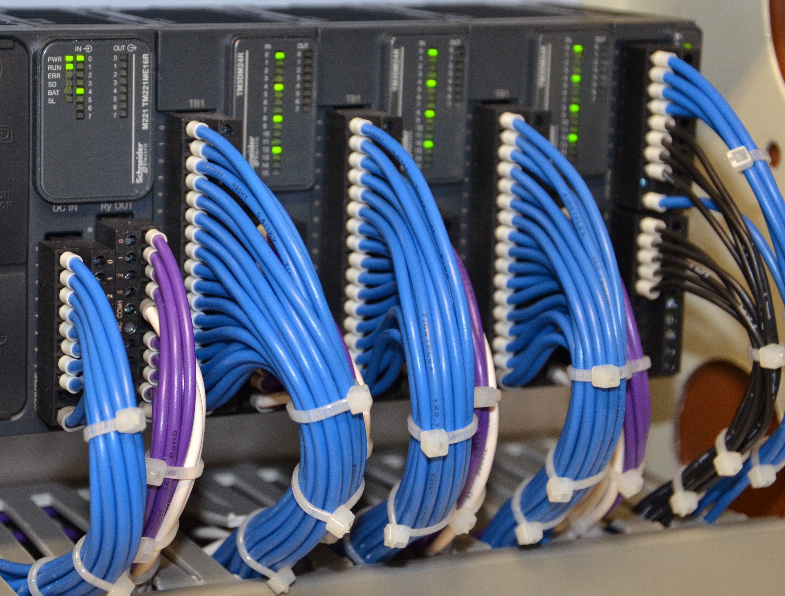 Bundles of blue, purple, black, and white wires organized and tied inside a control panel.