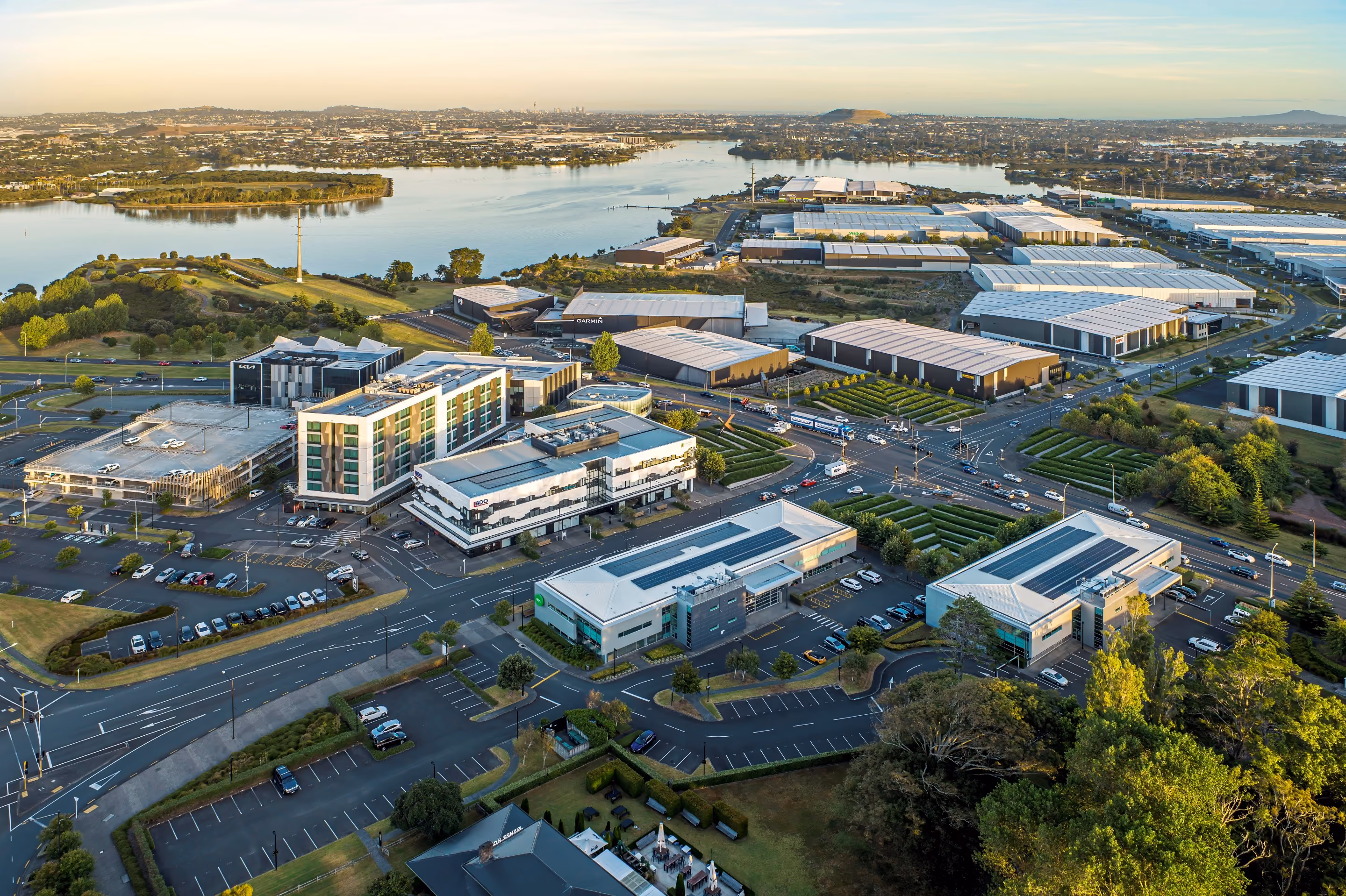 Aerial view of a modern business park with office buildings, roads, parking lots, and a river in the background.